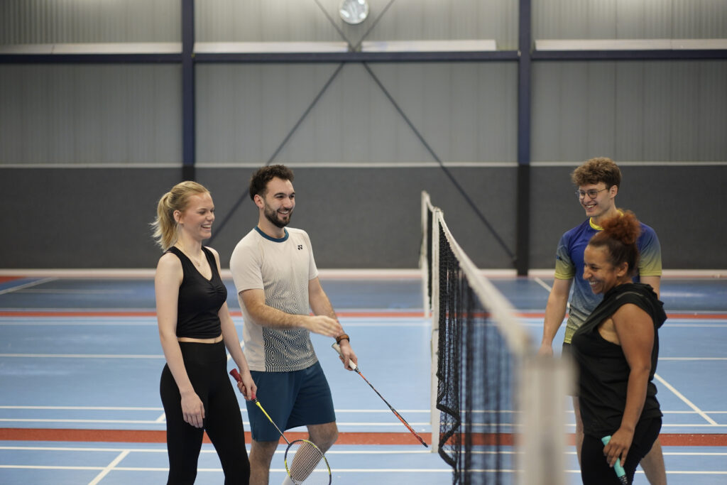 „Vier Badmintonspieler kommen lachend zum Netz, um sich nach einer Partie in der Tivoli Sports Halle zu bedanken.“